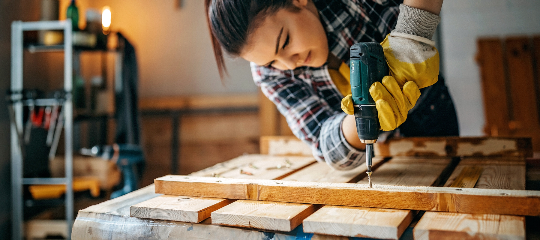 A woman using a power drill to place a wood screw into a piece of lumber.